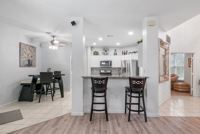 kitchen with white cabinetry, light stone counters, light tile patterned floors, appliances with stainless steel finishes, and kitchen peninsula