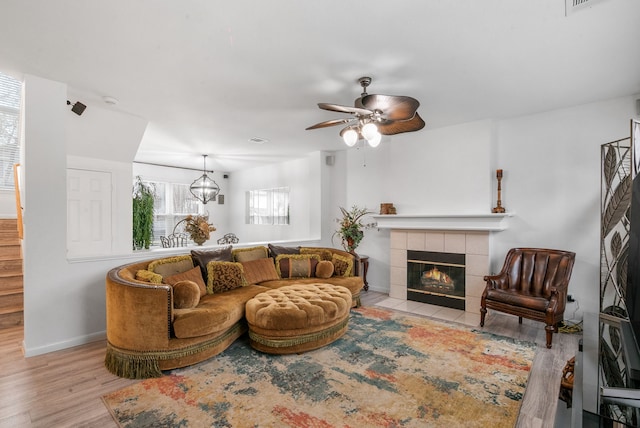 living room featuring a tile fireplace, ceiling fan, and light wood-type flooring