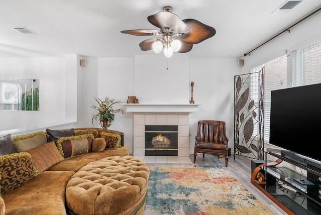 living room with light hardwood / wood-style floors, a tile fireplace, and ceiling fan