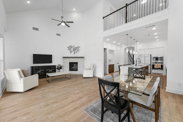 dining space with ceiling fan with notable chandelier, sink, light hardwood / wood-style floors, and a high ceiling