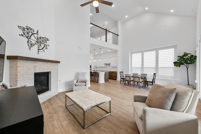 living room featuring high vaulted ceiling, a fireplace, sink, ceiling fan, and light wood-type flooring