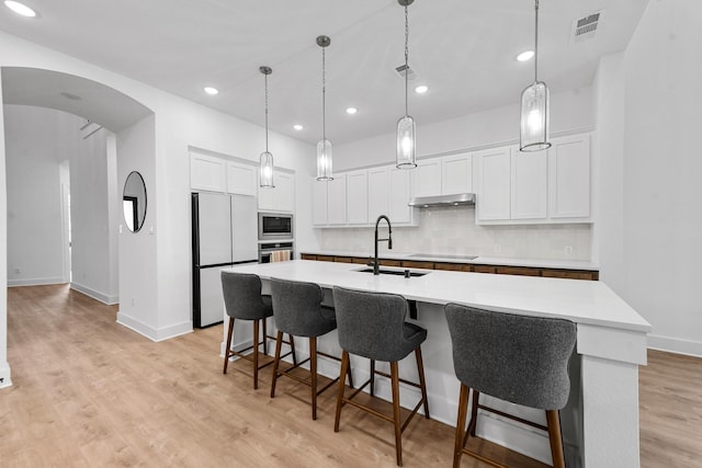 kitchen featuring white cabinetry, built in appliances, and a center island with sink