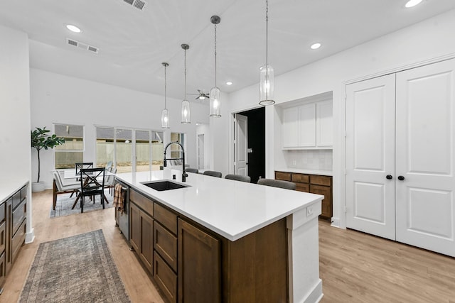 kitchen with sink, hanging light fixtures, a kitchen island with sink, stainless steel dishwasher, and light hardwood / wood-style floors