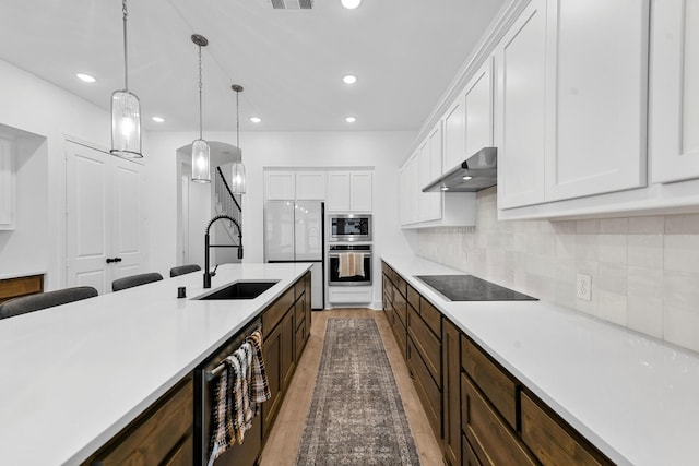 kitchen featuring sink, hanging light fixtures, black electric cooktop, range hood, and white cabinets