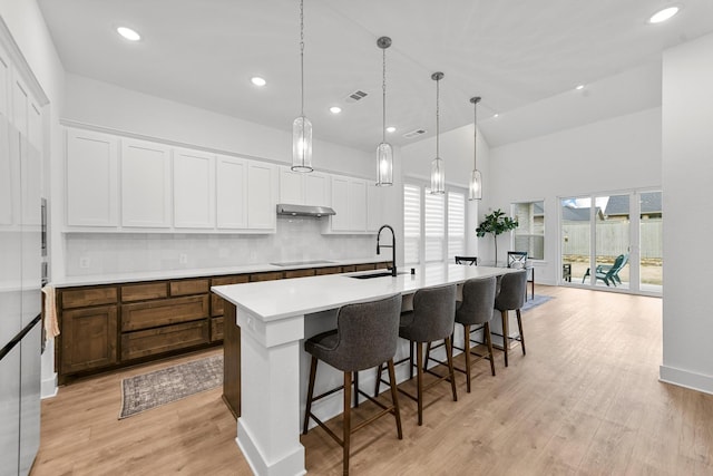 kitchen featuring black electric cooktop, decorative light fixtures, an island with sink, and white cabinets