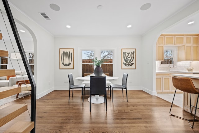 dining room with light wood finished floors, visible vents, arched walkways, crown molding, and baseboards