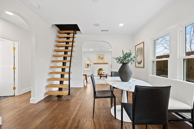 dining room featuring arched walkways, crown molding, stairs, and dark wood-style floors