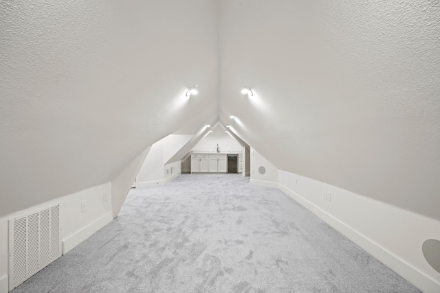 additional living space featuring vaulted ceiling, visible vents, light carpet, baseboards, and a textured ceiling