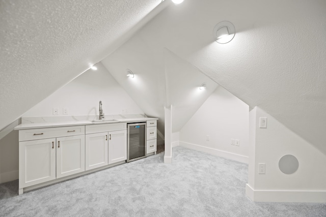 additional living space with a sink, a textured ceiling, light colored carpet, lofted ceiling, and beverage cooler