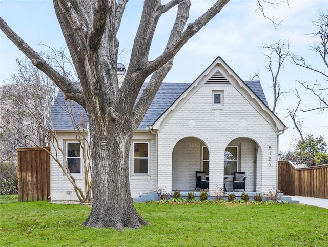 english style home with brick siding, a front yard, covered porch, and fence