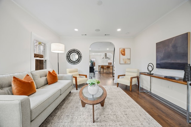 living area featuring dark wood finished floors, arched walkways, ornamental molding, and visible vents