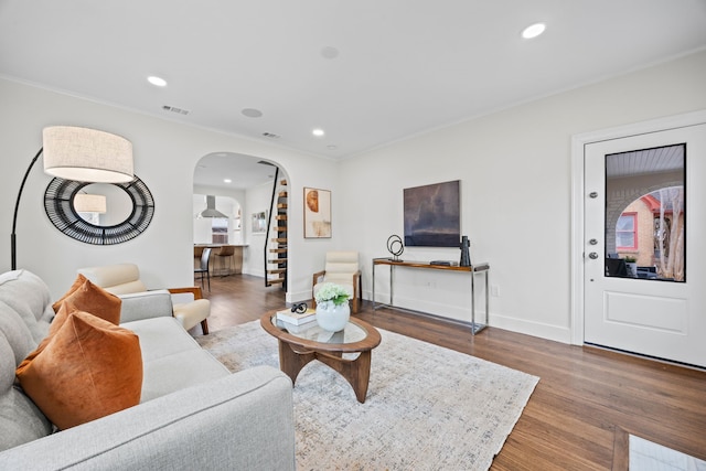 living room featuring crown molding, wood finished floors, arched walkways, baseboards, and visible vents