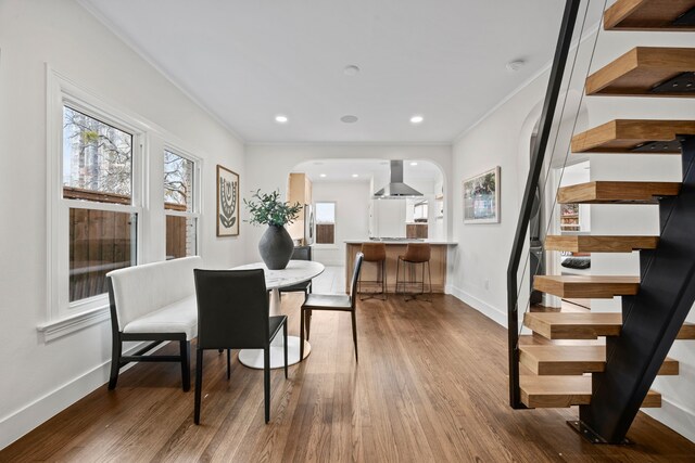 dining room featuring stairway, wood finished floors, arched walkways, baseboards, and ornamental molding