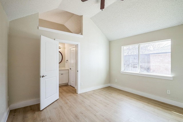 unfurnished bedroom with lofted ceiling, ensuite bathroom, light hardwood / wood-style flooring, and a textured ceiling