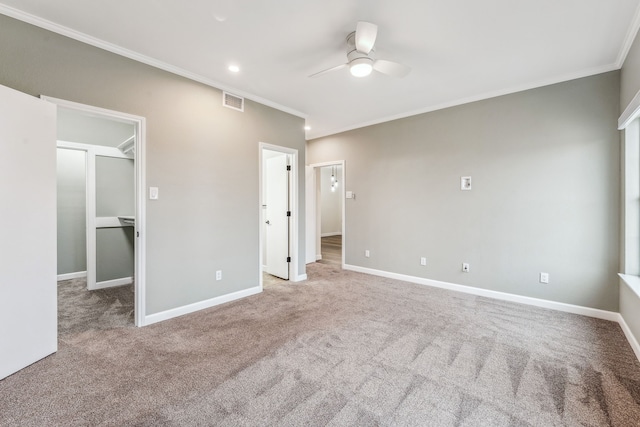 unfurnished bedroom featuring ceiling fan, a walk in closet, ornamental molding, and light colored carpet