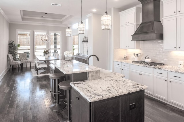 kitchen with white cabinetry, stainless steel gas cooktop, custom exhaust hood, and a center island with sink