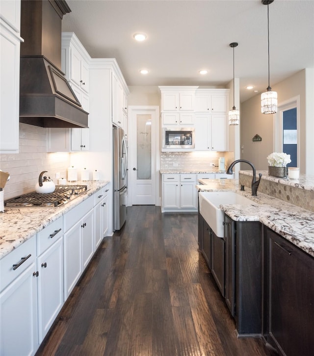 kitchen with sink, appliances with stainless steel finishes, white cabinetry, hanging light fixtures, and premium range hood