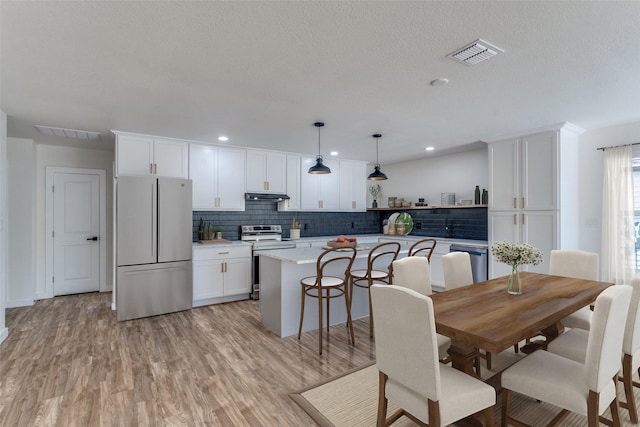 kitchen featuring a kitchen island, appliances with stainless steel finishes, pendant lighting, white cabinets, and light stone countertops