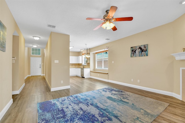 living room featuring wood-type flooring, sink, ceiling fan with notable chandelier, and a textured ceiling