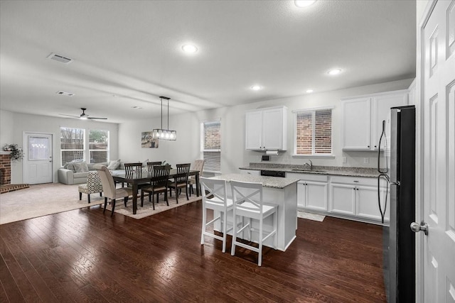 kitchen featuring white cabinetry, decorative light fixtures, stainless steel refrigerator, and a kitchen island