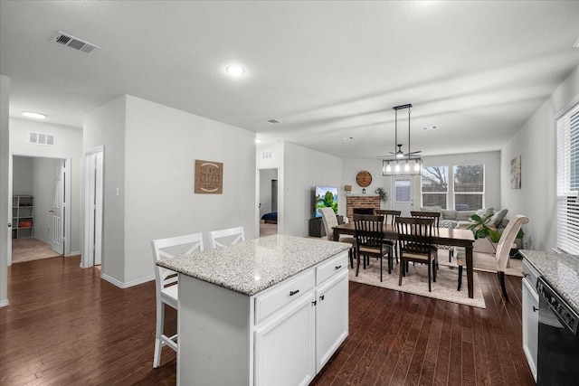 kitchen with a kitchen bar, a center island, hanging light fixtures, a fireplace, and white cabinets