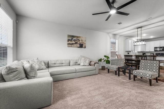 carpeted living room featuring ceiling fan with notable chandelier