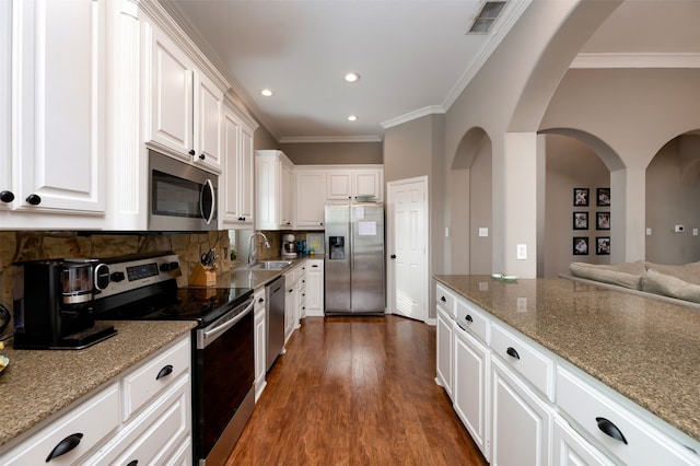 kitchen with sink, appliances with stainless steel finishes, white cabinetry, ornamental molding, and light stone countertops