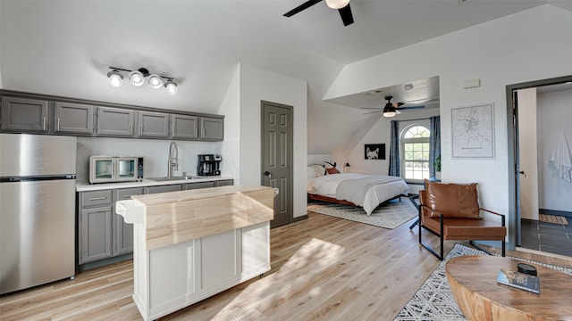 bedroom featuring vaulted ceiling, light wood-style flooring, freestanding refrigerator, and a sink