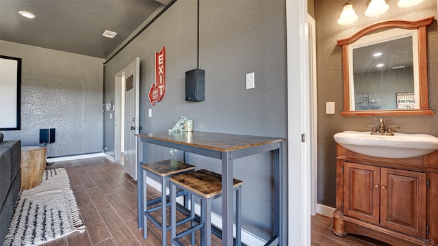 interior space featuring a textured wall, baseboards, wood tiled floor, and a sink