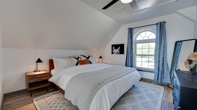 bedroom with light wood-type flooring, a ceiling fan, baseboards, attic access, and vaulted ceiling