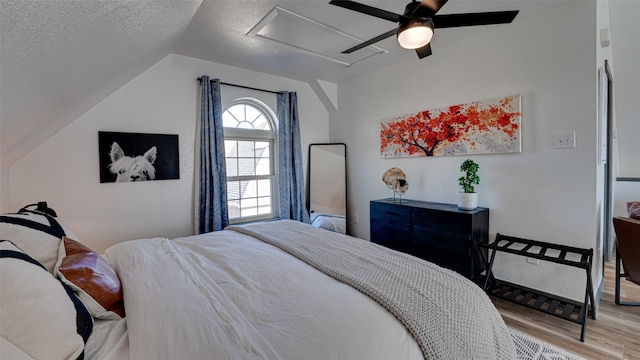 bedroom featuring wood finished floors, lofted ceiling, attic access, ceiling fan, and a textured ceiling