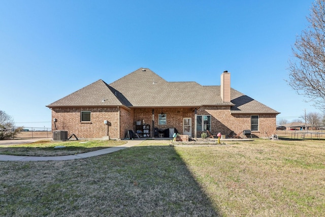 rear view of house featuring a lawn, a chimney, brick siding, and fence