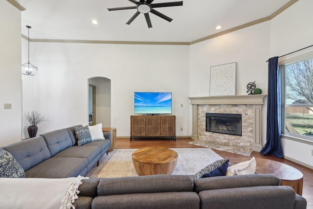 living room with arched walkways, a stone fireplace, ornamental molding, and wood finished floors