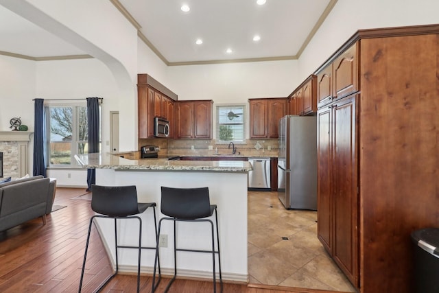 kitchen featuring a sink, backsplash, stainless steel appliances, a peninsula, and crown molding