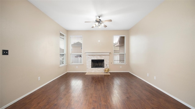 unfurnished living room featuring a stone fireplace, dark wood-type flooring, and ceiling fan