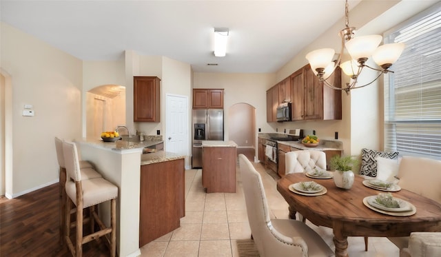 kitchen with light tile patterned floors, a breakfast bar, hanging light fixtures, stainless steel appliances, and kitchen peninsula