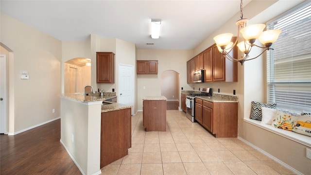 kitchen with appliances with stainless steel finishes, light stone countertops, light tile patterned flooring, decorative light fixtures, and kitchen peninsula