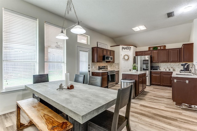 dining space featuring lofted ceiling, sink, a textured ceiling, and light wood-type flooring