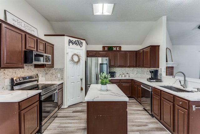 kitchen featuring lofted ceiling, sink, light hardwood / wood-style flooring, stainless steel appliances, and a kitchen island