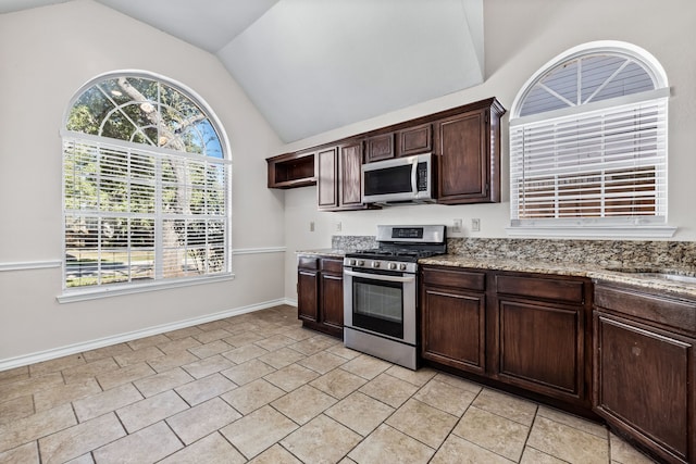 kitchen with light stone counters, vaulted ceiling, dark brown cabinets, light tile patterned floors, and appliances with stainless steel finishes