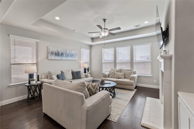 living room featuring dark wood-type flooring, ceiling fan, plenty of natural light, and a tray ceiling