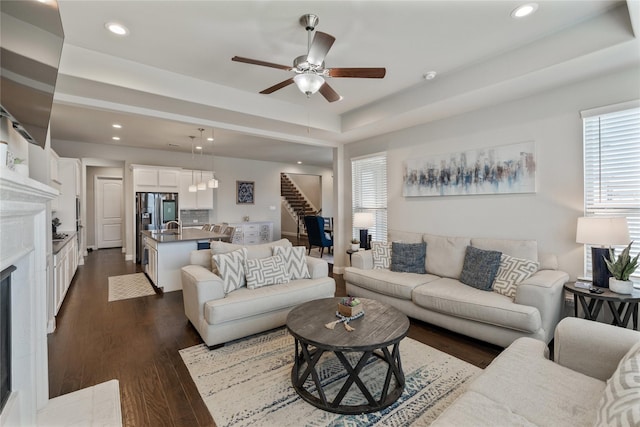 living room with dark hardwood / wood-style flooring, a raised ceiling, a premium fireplace, and ceiling fan