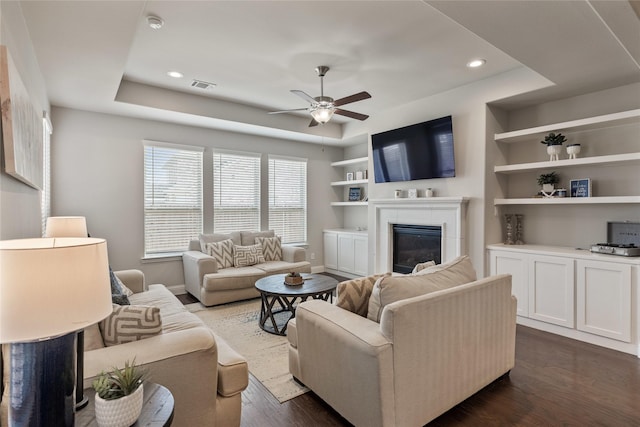 living room with ceiling fan, a tray ceiling, dark wood-type flooring, and built in shelves