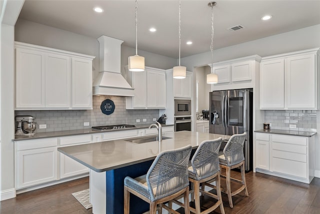 kitchen featuring premium range hood, sink, white cabinetry, decorative light fixtures, and appliances with stainless steel finishes