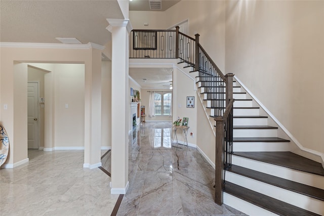 foyer entrance featuring a towering ceiling, ornamental molding, decorative columns, and ceiling fan