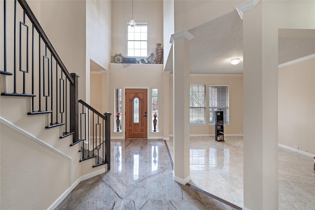 entrance foyer with decorative columns, ornamental molding, a towering ceiling, and a textured ceiling