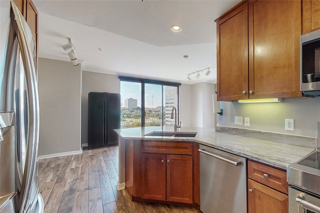 kitchen featuring sink, appliances with stainless steel finishes, light stone counters, light hardwood / wood-style floors, and kitchen peninsula