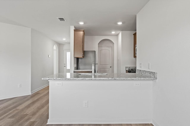 kitchen featuring sink, stainless steel fridge, light stone counters, and kitchen peninsula