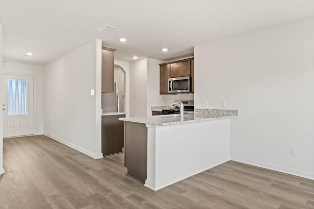 kitchen featuring appliances with stainless steel finishes, light stone countertops, kitchen peninsula, and light wood-type flooring