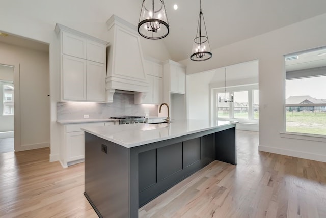 kitchen with white cabinetry, hanging light fixtures, a notable chandelier, an island with sink, and custom range hood